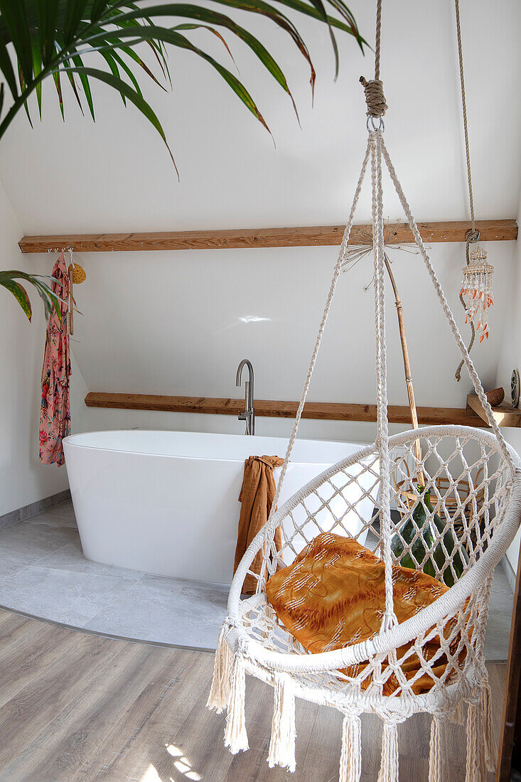 Freestanding bathtub and hanging chair in bathroom with wooden details