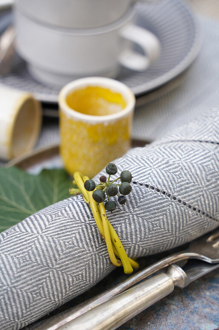 Table decoration with patterned cloth napkin, yellow napkin ring made of twigs with ivy berries