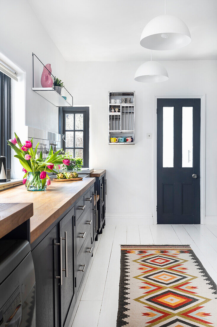 Narrow kitchen with dark cabinets, wooden worktop and colourful patterned carpet