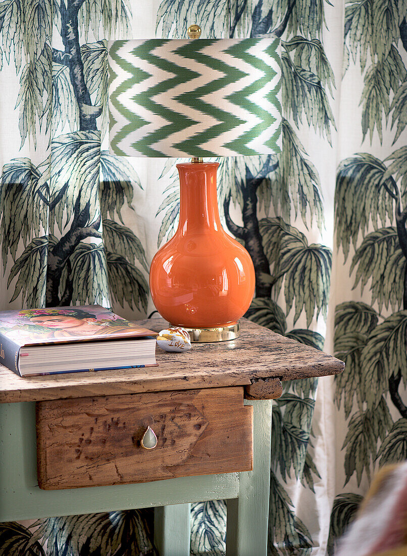 Orange-coloured table lamp with patterned shade on a rustic wooden table