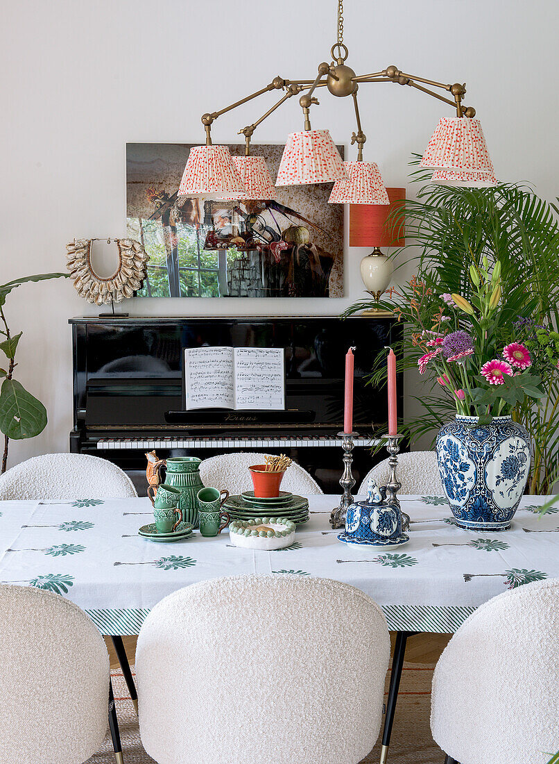 Dining table with patterned tablecloth in front of black piano, large ceiling light