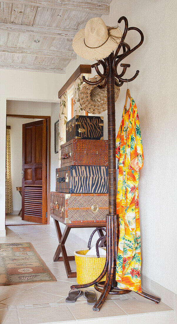 Hallway with wooden clothes rack, straw hat and patterned suitcase stack