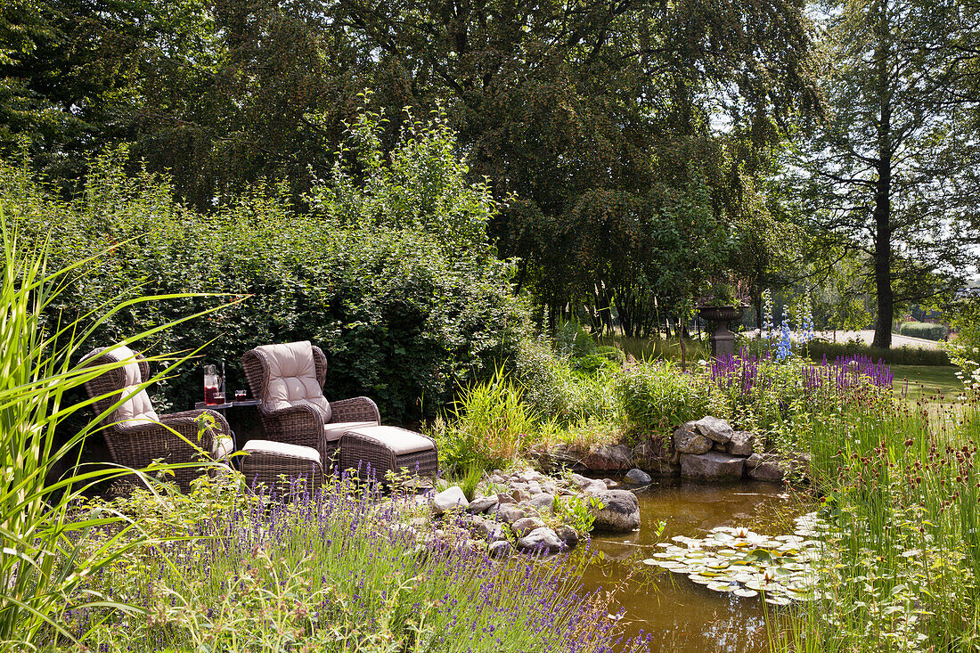 Sitzecke mit Rattansesseln neben Teich im sommerlichen Garten