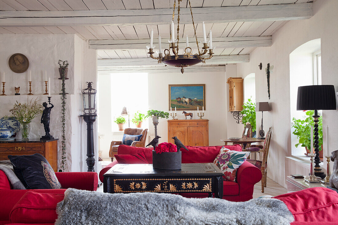 Wohnzimmer im Landhausstil mit roten Sofas, Sesseln und antikem Kronleuchter