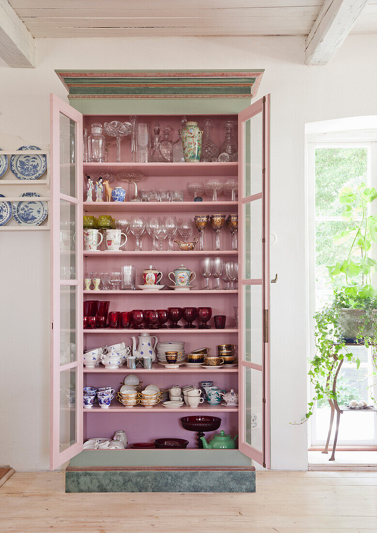 Display cabinet with pink interior, filled with porcelain and crystal glasses