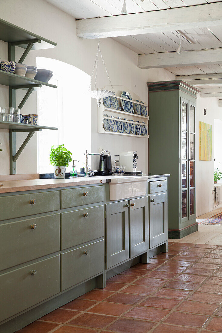 Country-style kitchen with olive green cupboards and terracotta tiles