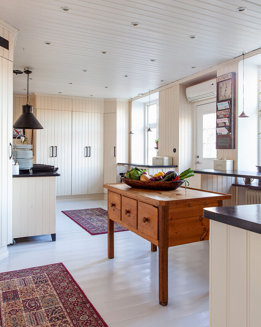 Country-style kitchen with wooden table and fruit bowl and Persian rugs on a white floor