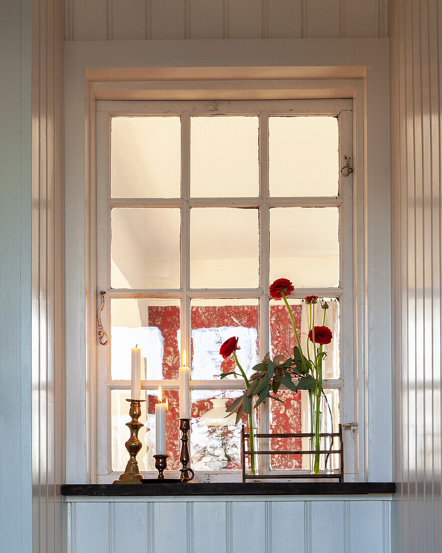 Fensterbank mit Kerzenleuchtern und roten Blumen in Glasvase