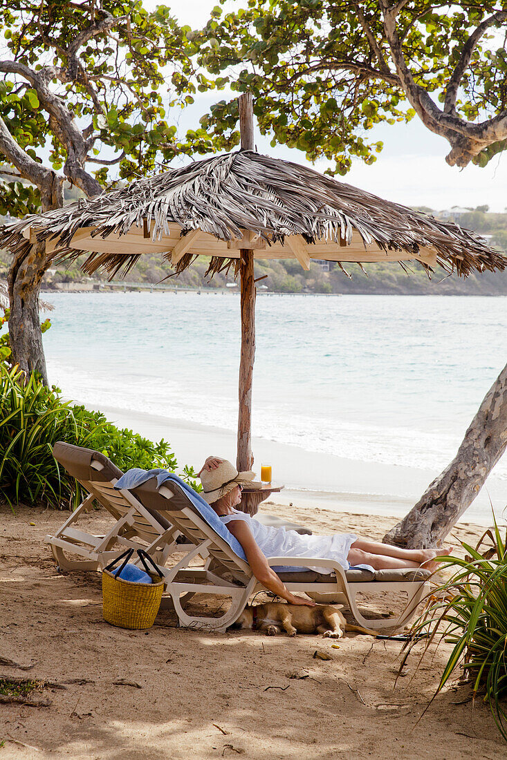 Woman enjoying an idyllic holiday on the beach on a sun lounger under a thatched umbrella