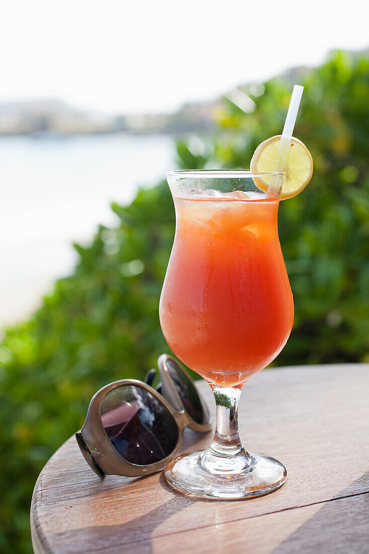 Sommerlicher Cocktail mit Zitronenscheibe und Sonnenbrille auf Holztisch