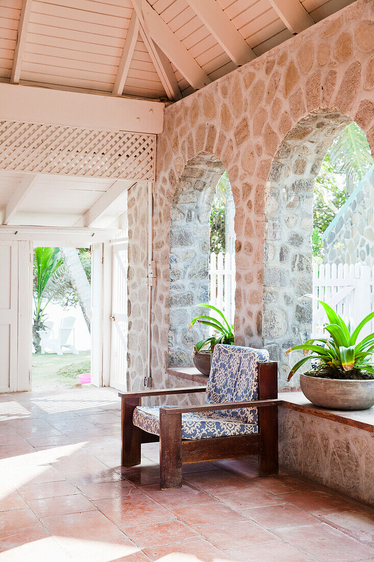 Interior with stone walls, wooden armchair with patterned cushions and potted plants