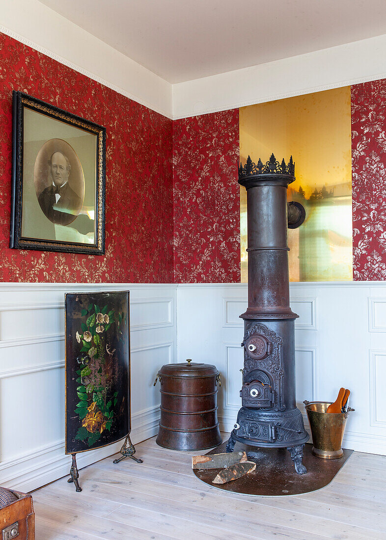 Antique stove and coal bucket in front of red patterned wallpaper and white wood panelling