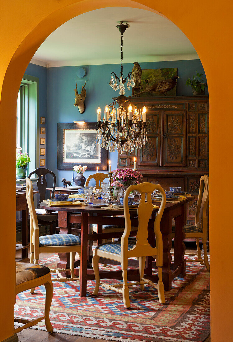 Dining room with chandelier, rustic wooden furniture and colorful patterned carpet