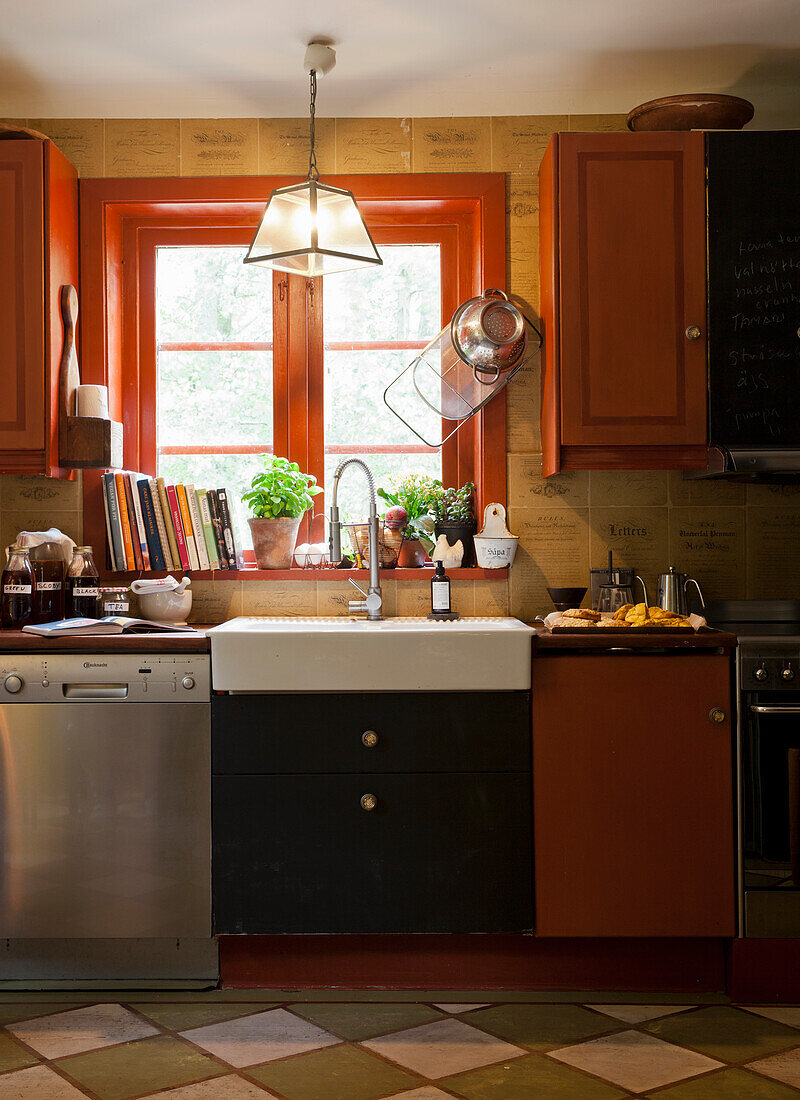 Kitchen with red wooden cupboards and window above sink