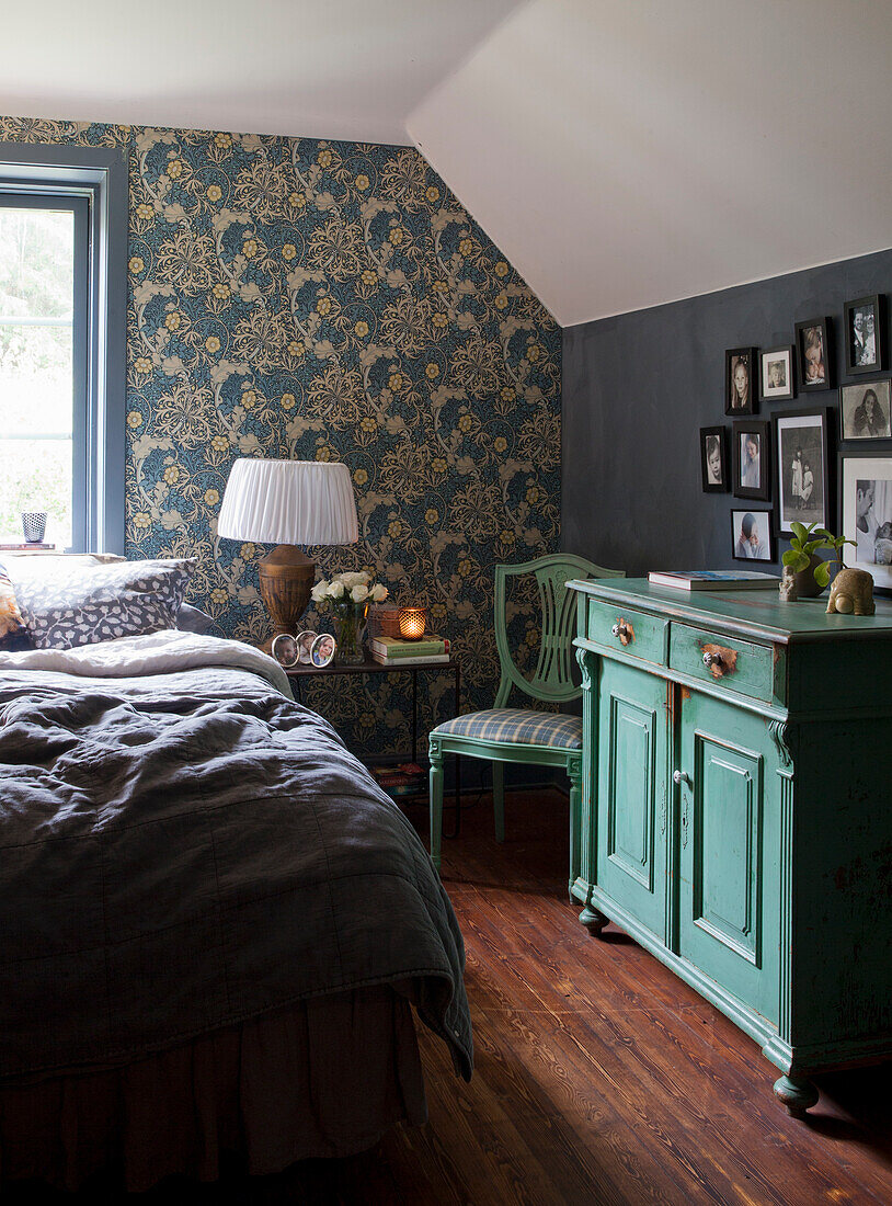 Bedroom with floral wallpaper, antique green chest of drawers and wooden floor