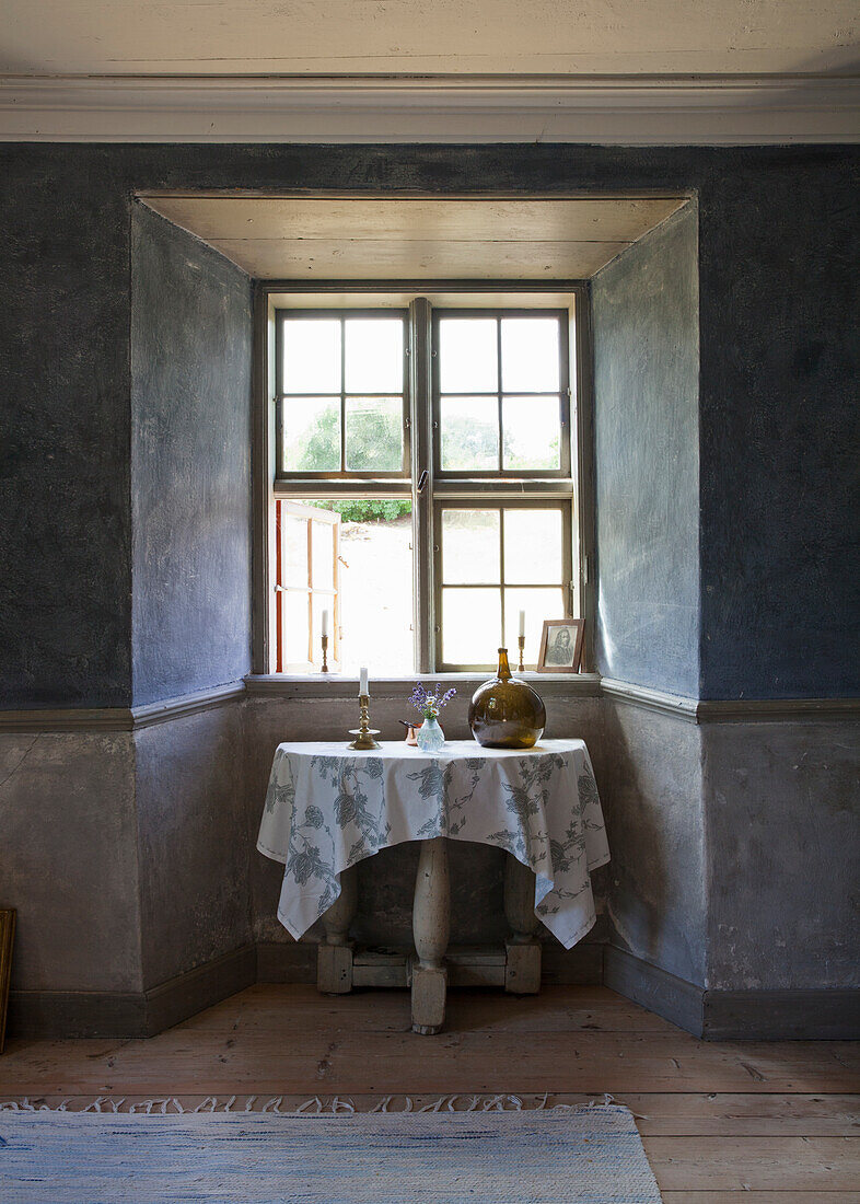 Small wooden table with flowered tablecloth in front of rustic bay window