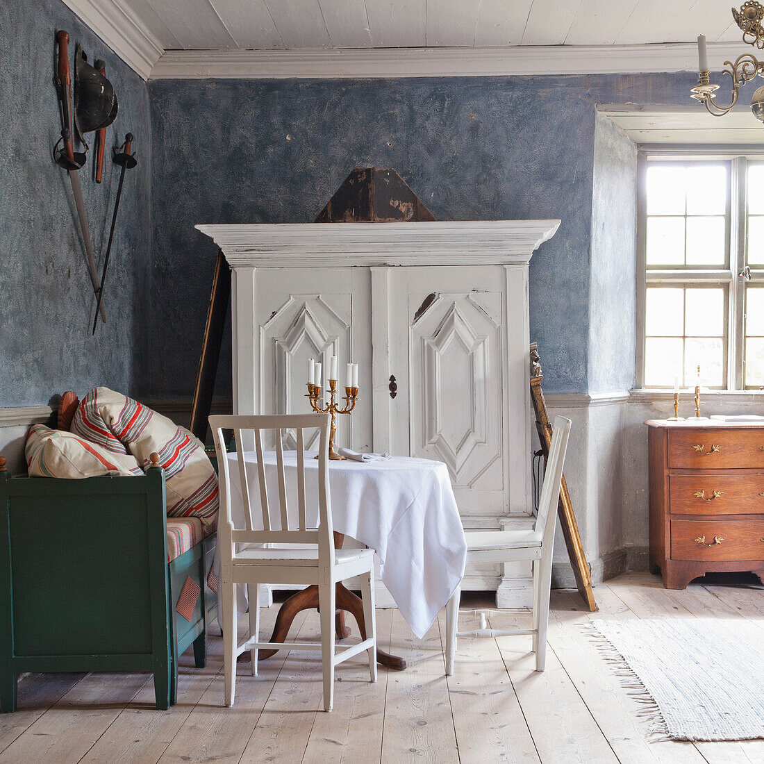 Essbereich im Vintage-Look mit weißem Tisch, Stühlen und antikem Schrank vor blauer Wand