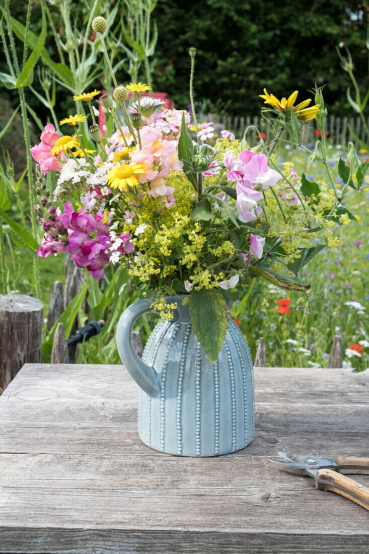 Bunte Sommerblumen in blauer Keramikvase auf Holztisch im Garten