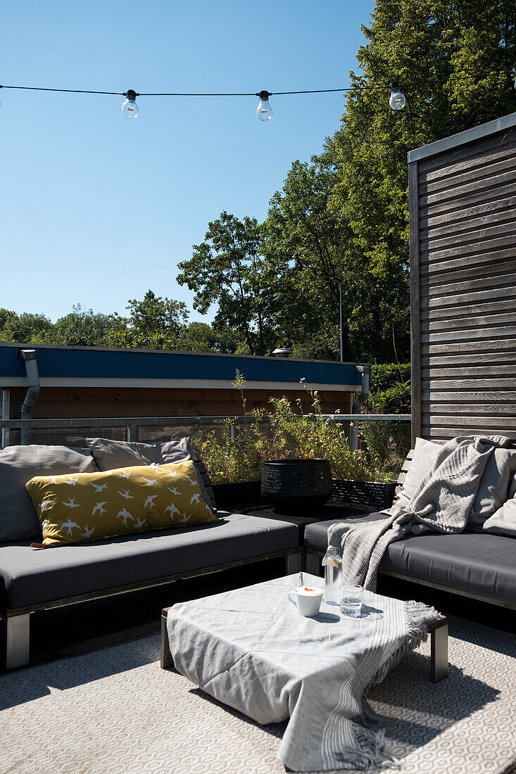 Sonnige Terrasse mit modernen Gartenmöbeln und Lichterkette