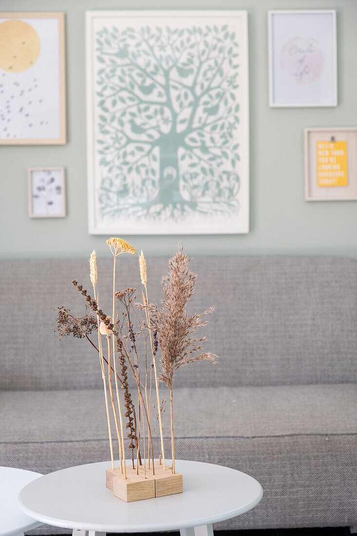 Dried flower arrangement on a round coffee table in front of a grey sofa and picture wall