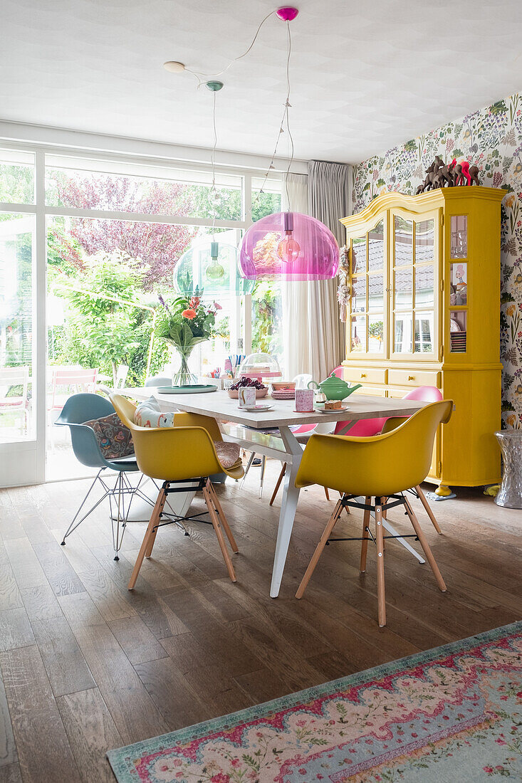 Dining room with yellow chairs, pink pendant light and yellow display cabinet