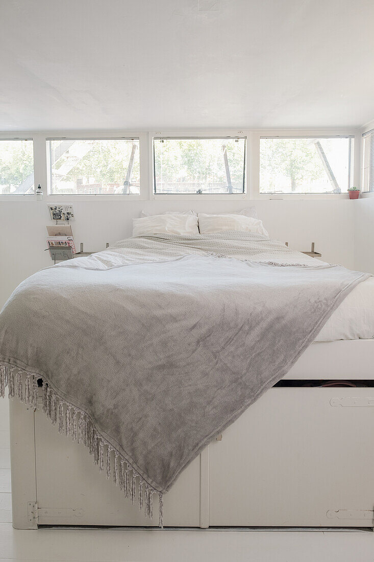 Bedroom with row of windows and light-coloured bed with grey ceiling