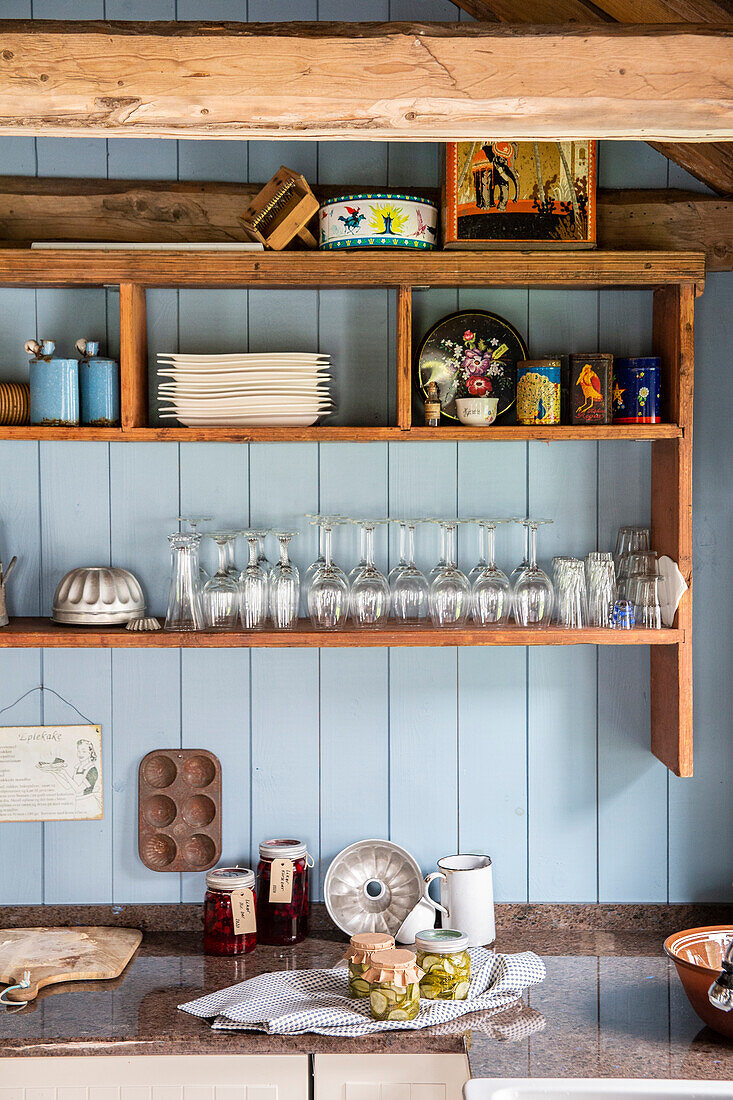 Open kitchen shelves with crockery and glasses in front of blue wood panelling