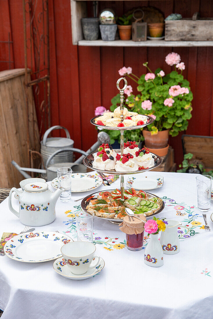 Etagere mit Gebäck und Sandwiches auf gedecktem Tisch im Garten