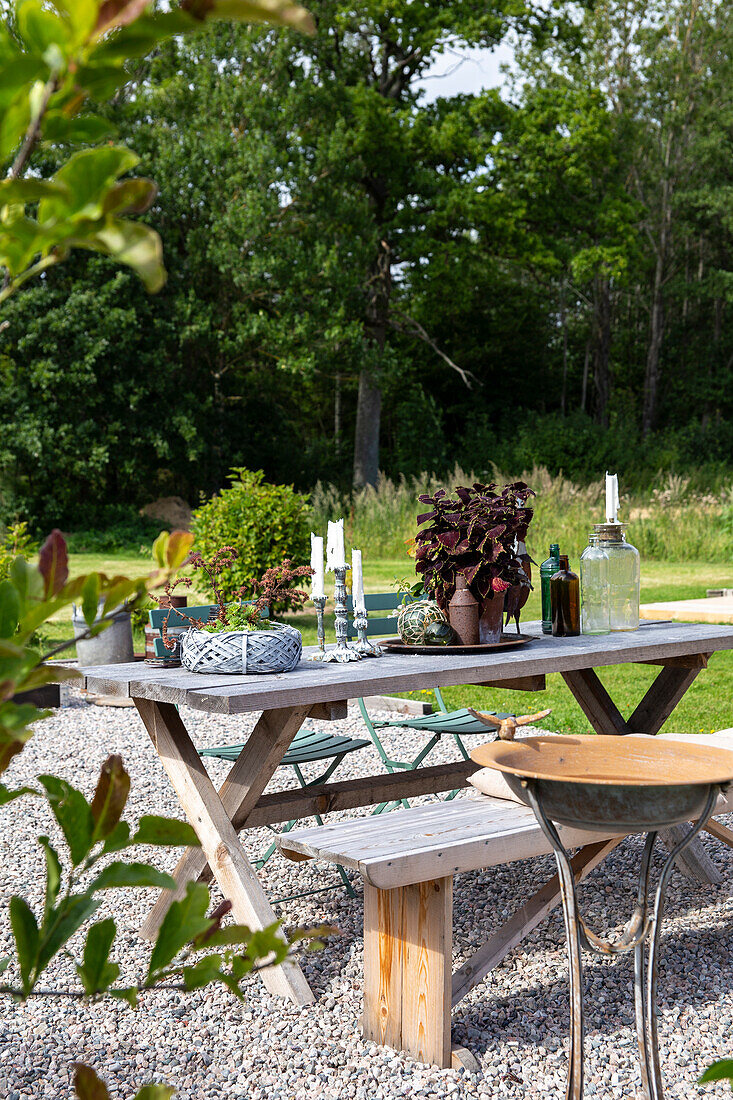 Holztisch mit Pflanzen und Kerzen auf Kiesfläche im Garten