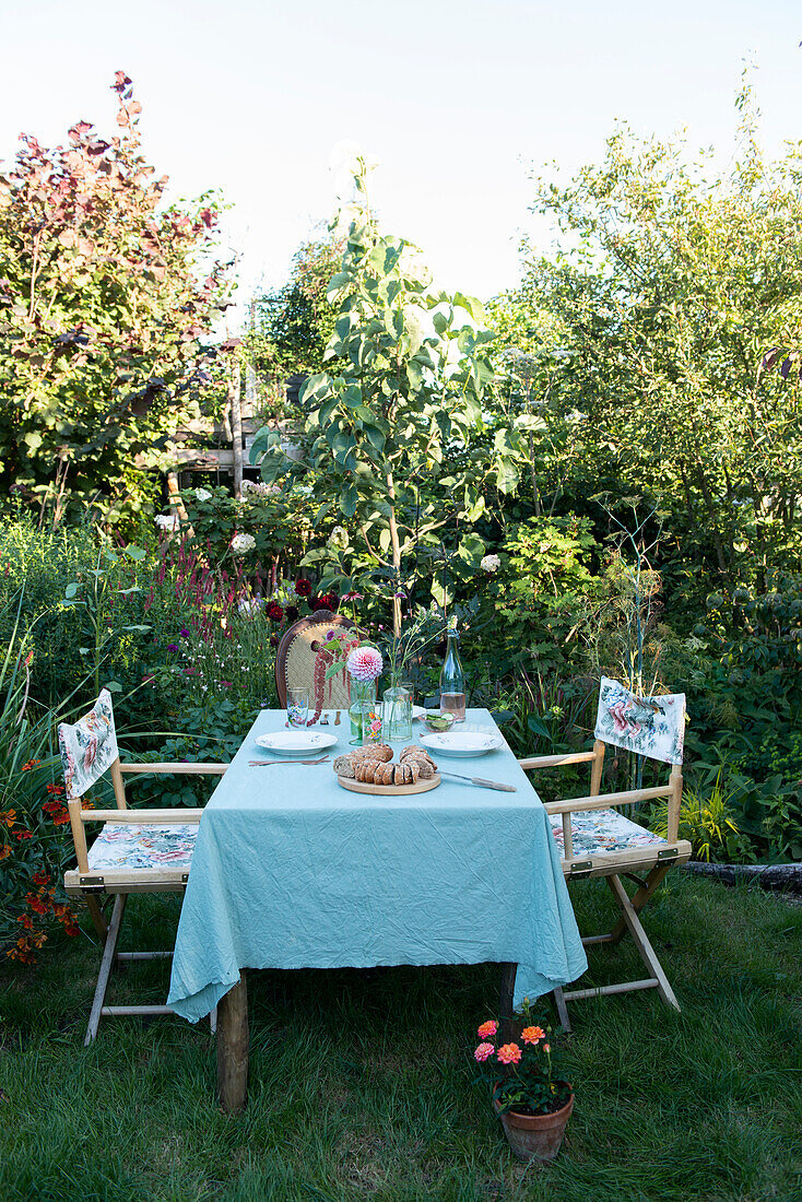 Gedeckter Gartentisch mit Gebäck und Blumen in sommerlicher Gartenumgebung