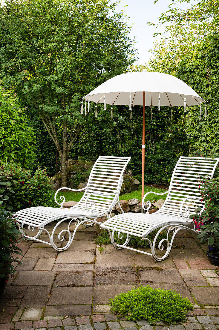 Two white garden loungers with parasol on a paved terrace