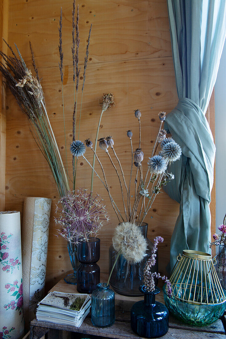 Dried flower arrangement in glass vases in front of wood panelling and curtains