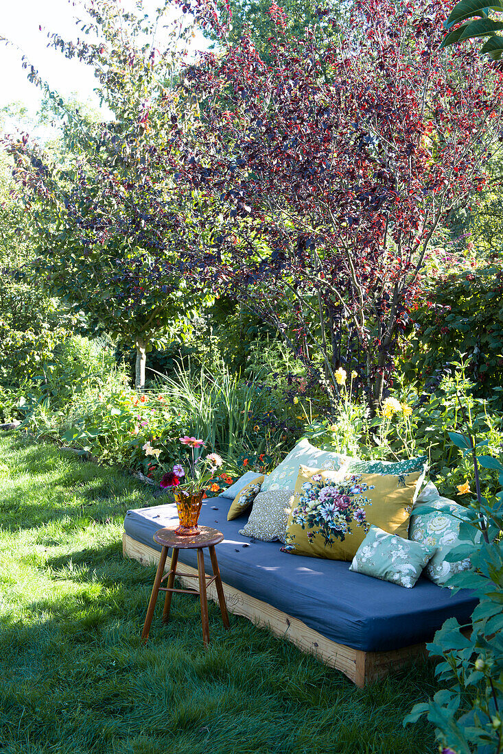 Gemütlicher Sitzbereich mit Holzsofa, Matratze und bunten Kissen im sommerlichen Garten