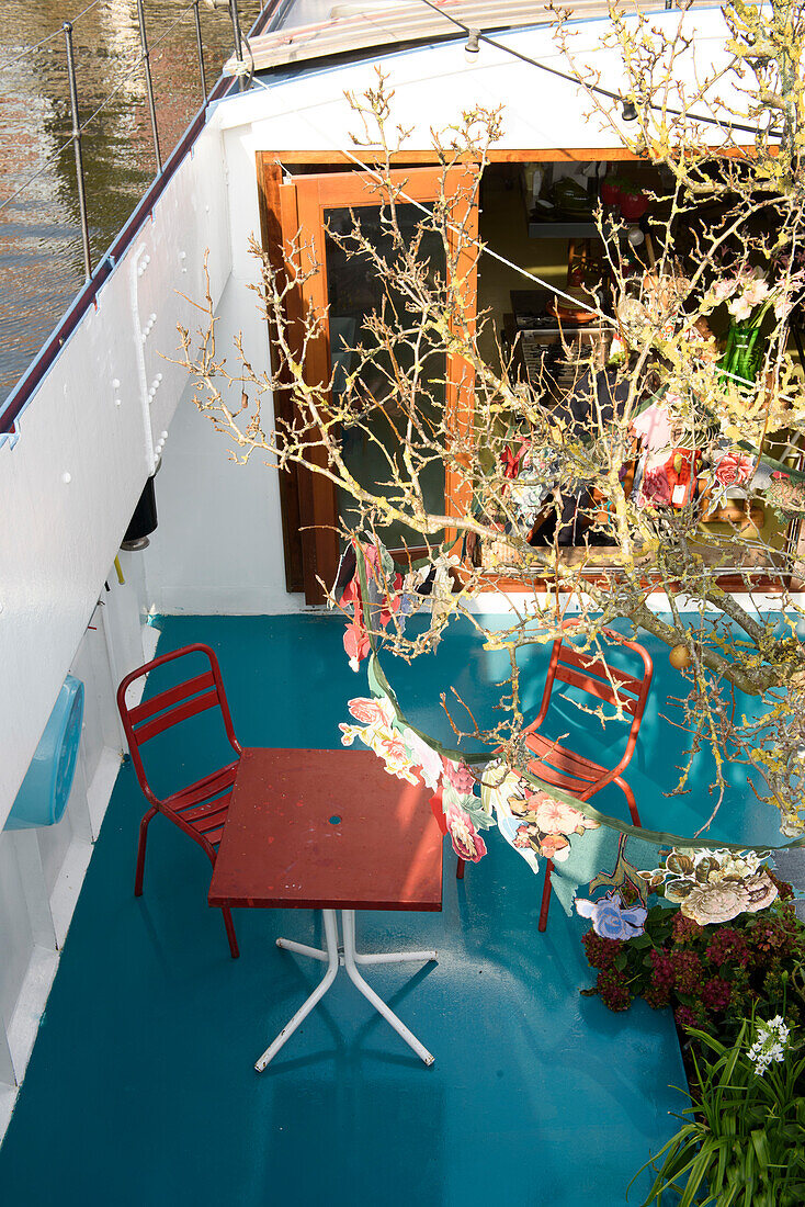 Bunt gestaltete Terrasse auf Hausboot mit roten Möbeln und blauem Boden