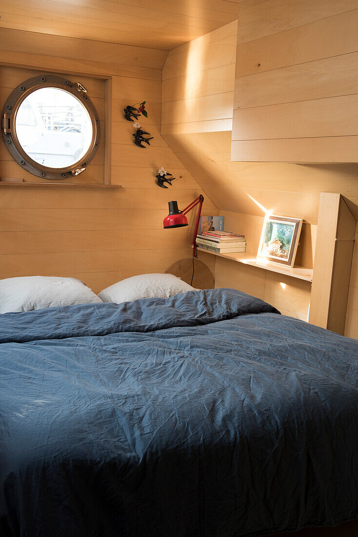 Wood-panelled bedroom with porthole window in the caravan