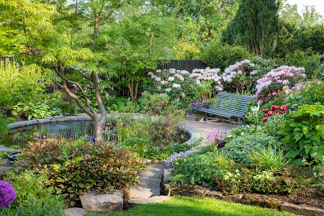 Idyllic garden with pond and wooden bench, surrounded by flowering shrubs