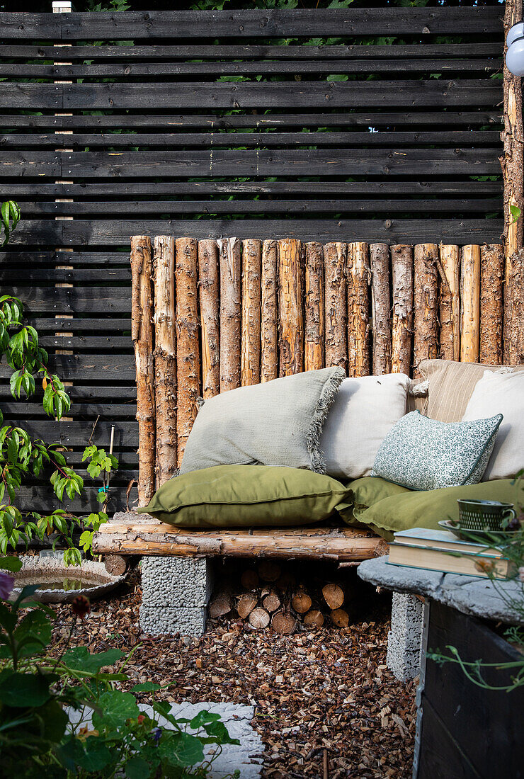 Seating area in the garden with wooden benches, cushions and privacy screen