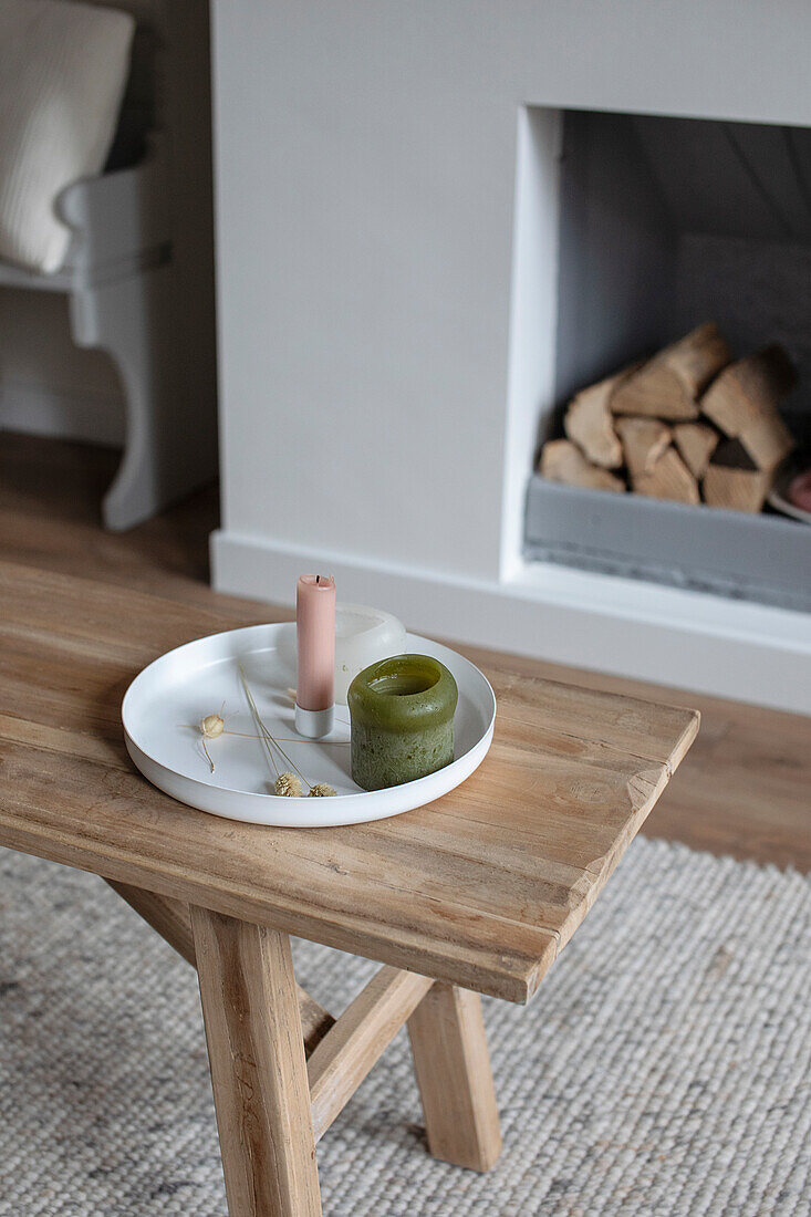 Holztisch mit Tablett und Kerzen vor Kamin mit Holzscheiten