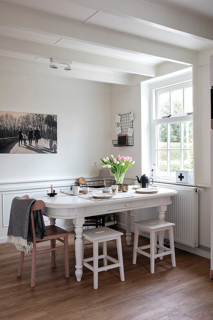 Country-style dining table with white wooden stools and bouquet of tulips by the window