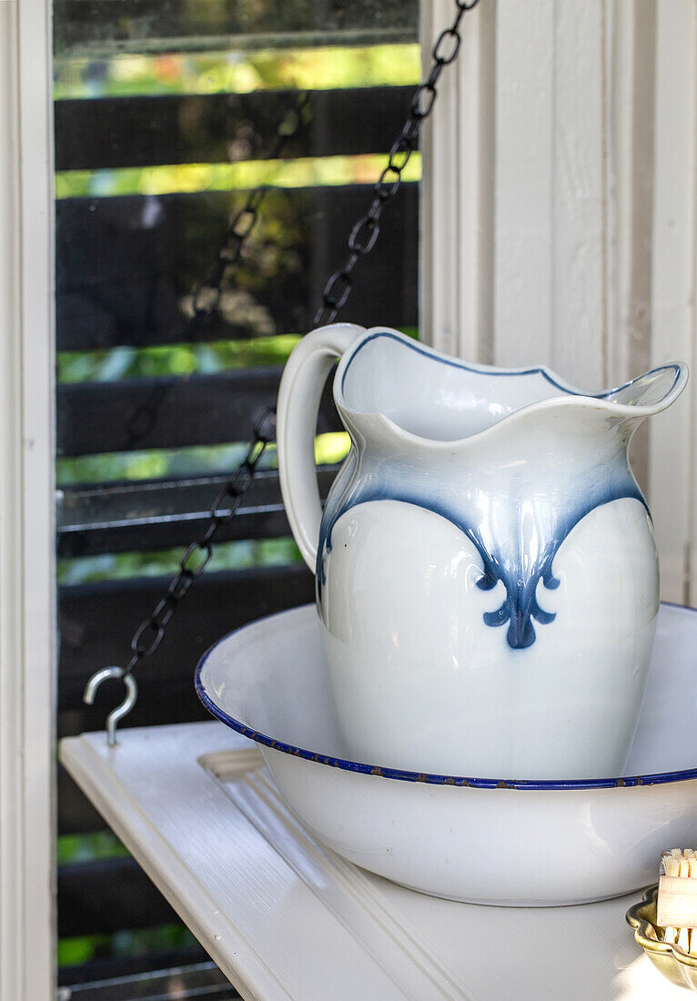 White jug with blue rim on matching wash bowl in front of window