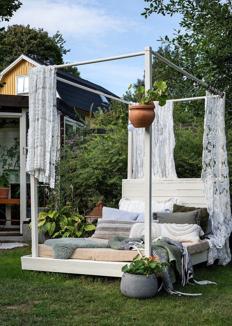 Lounge bed with lace curtains and cushions in the garden