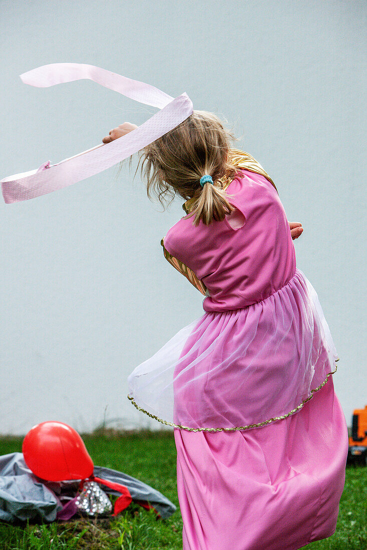 Child in a princess dress dances with a ribbon in the garden