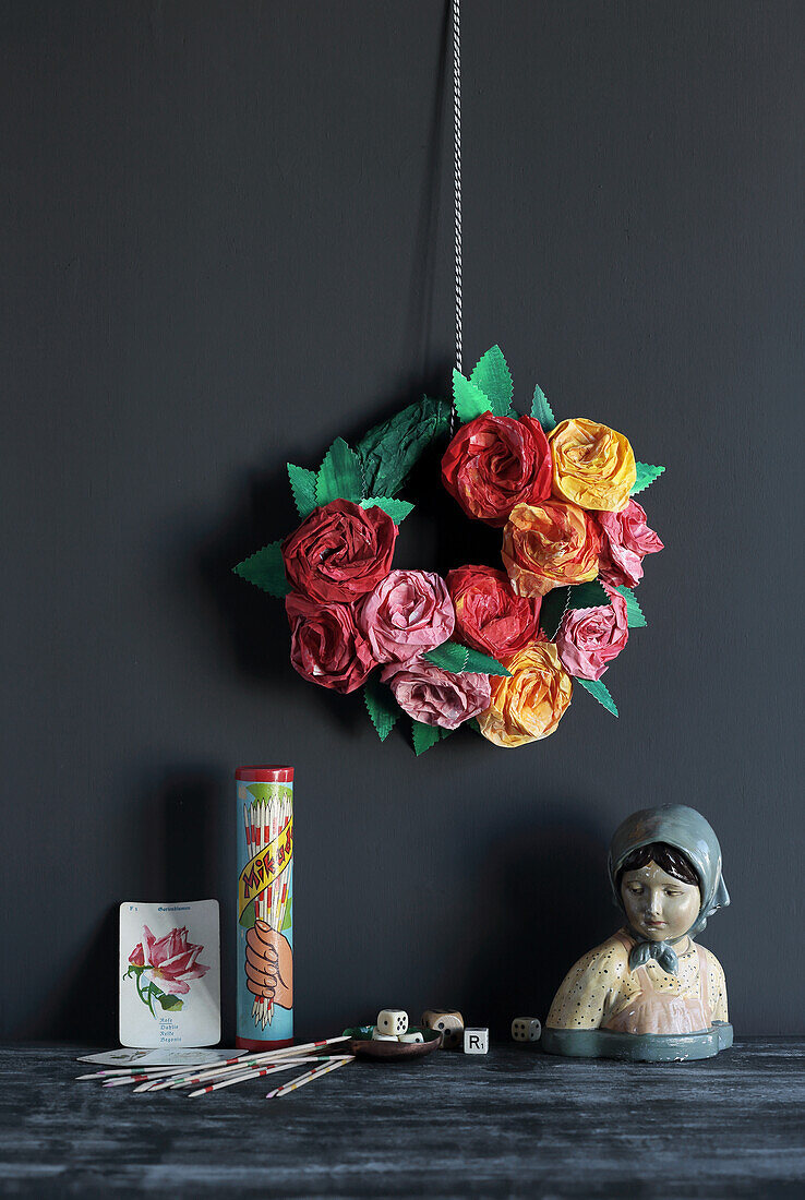 DIY-Papierkranz mit Papierrosen an dunkler Wand mit Vintage-Dekoration