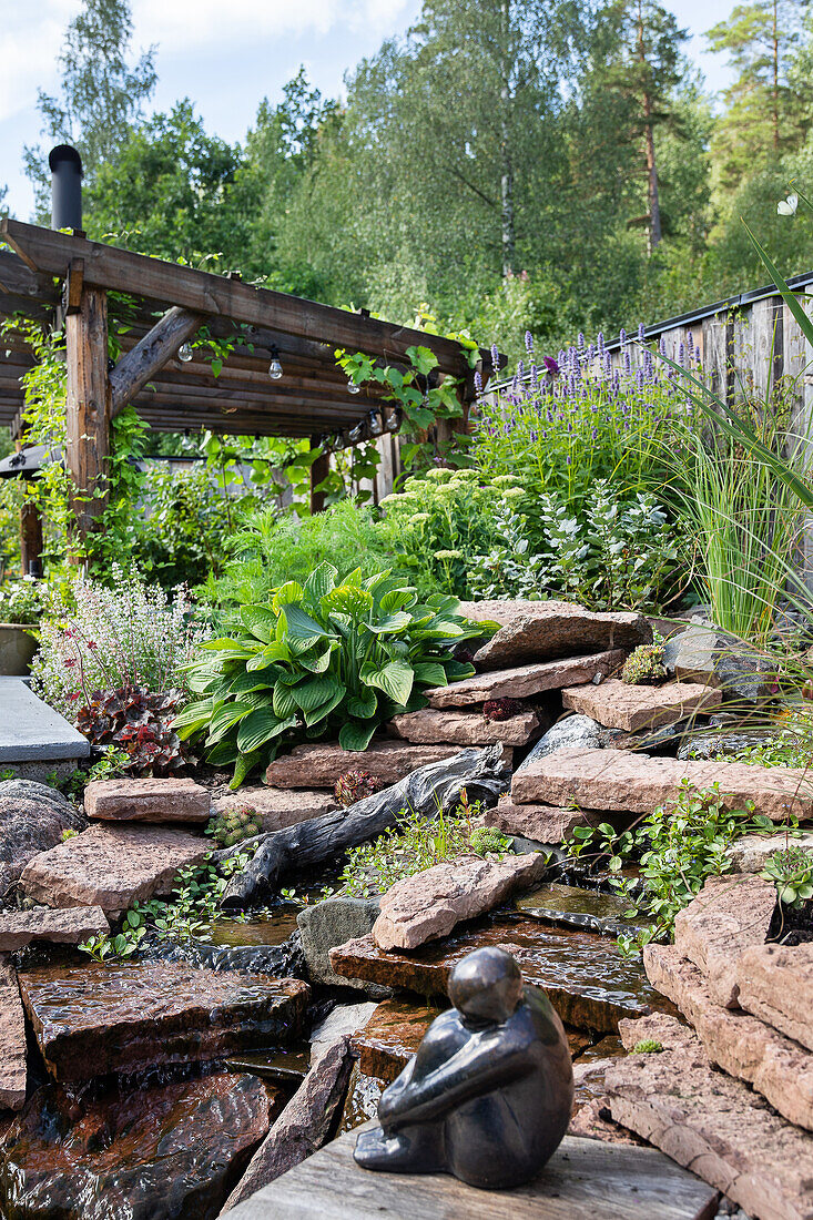 Steinlandschaft mit Wasserspiel und Skulptur im Garten