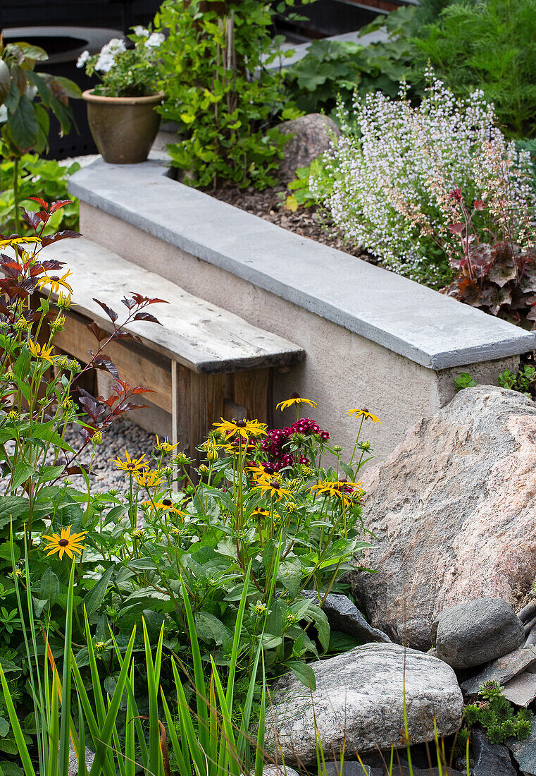 Stein- und Holzbank umgeben von Sommerblumen im Garten