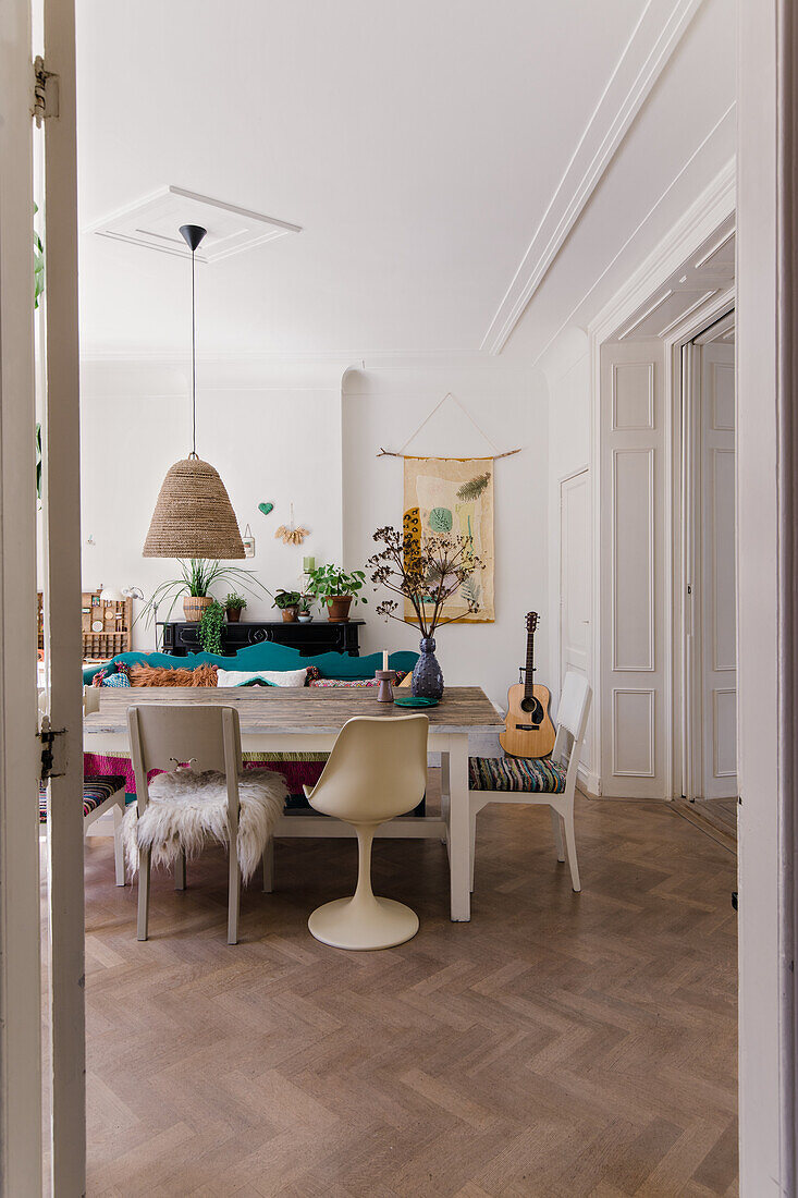 Dining area with wooden table, various chairs and rattan lamp, guitar leaning against the wall