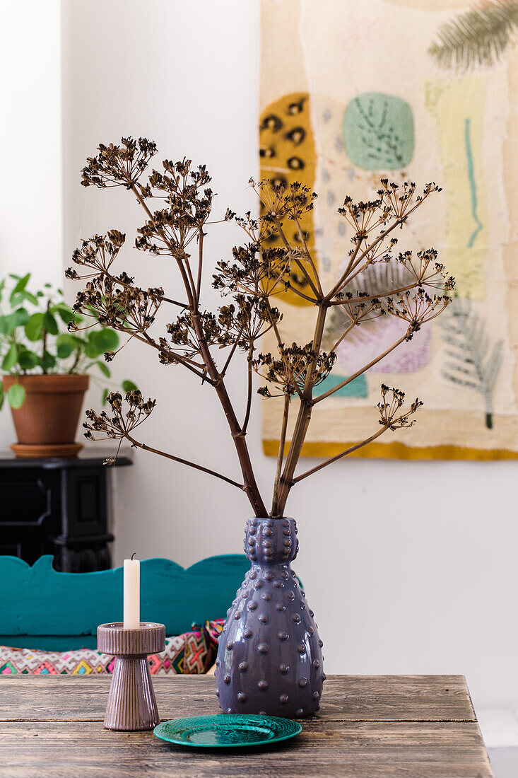 Ceramic vase with dried twigs on wooden table, candle holder next to it