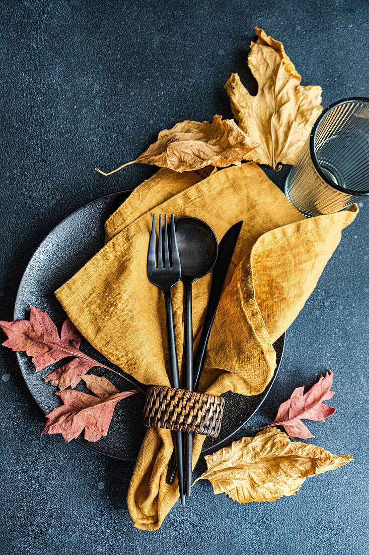 Herbstliches Tischgedeck mit getrockneten Blättern auf dunklem Hintergrund