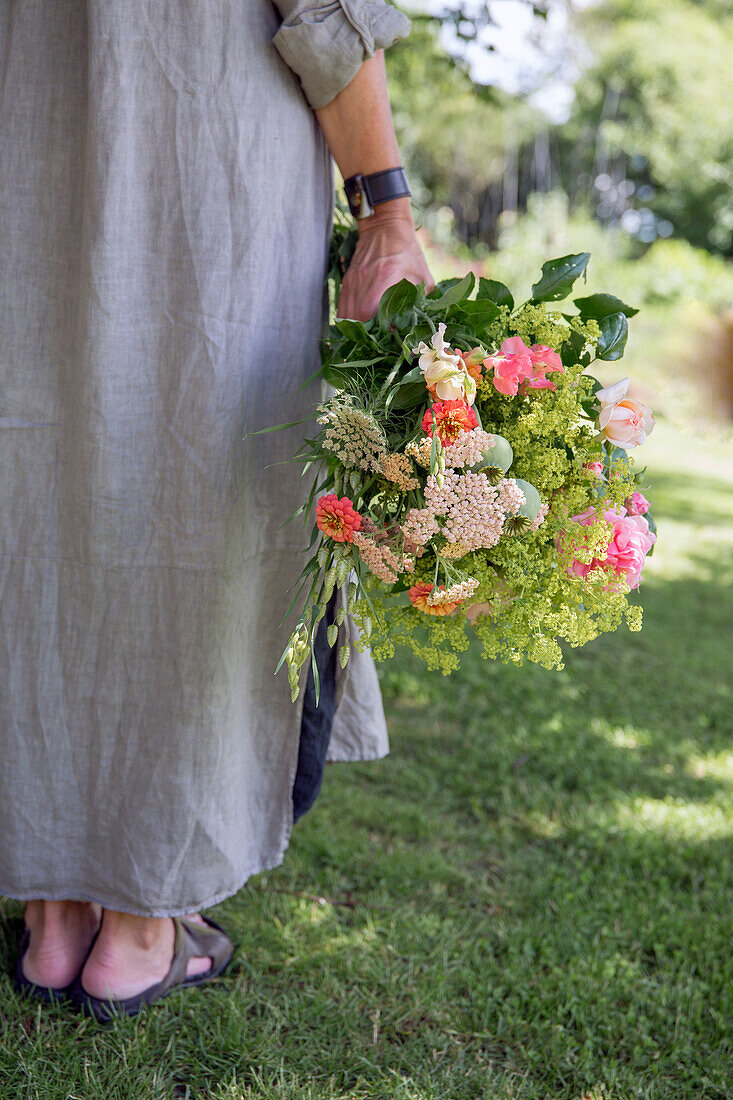 Woman in linen dress holds summer bouquet in the garden