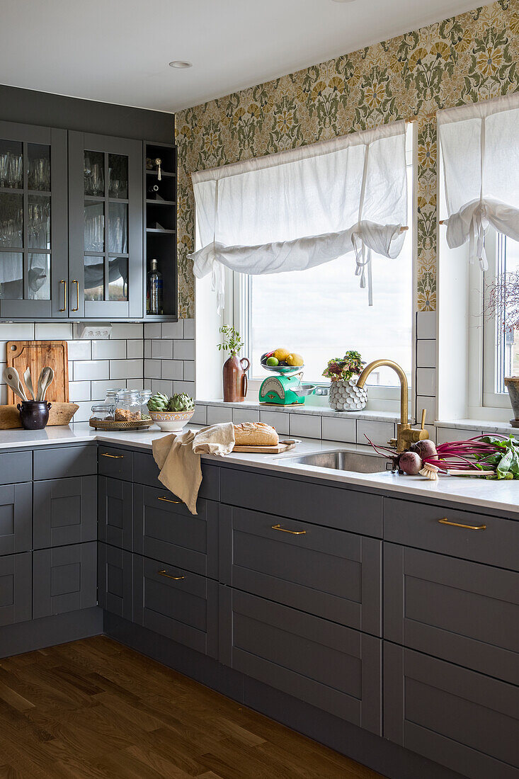 Kitchen with grey cupboards and floral wallpaper above the sink area